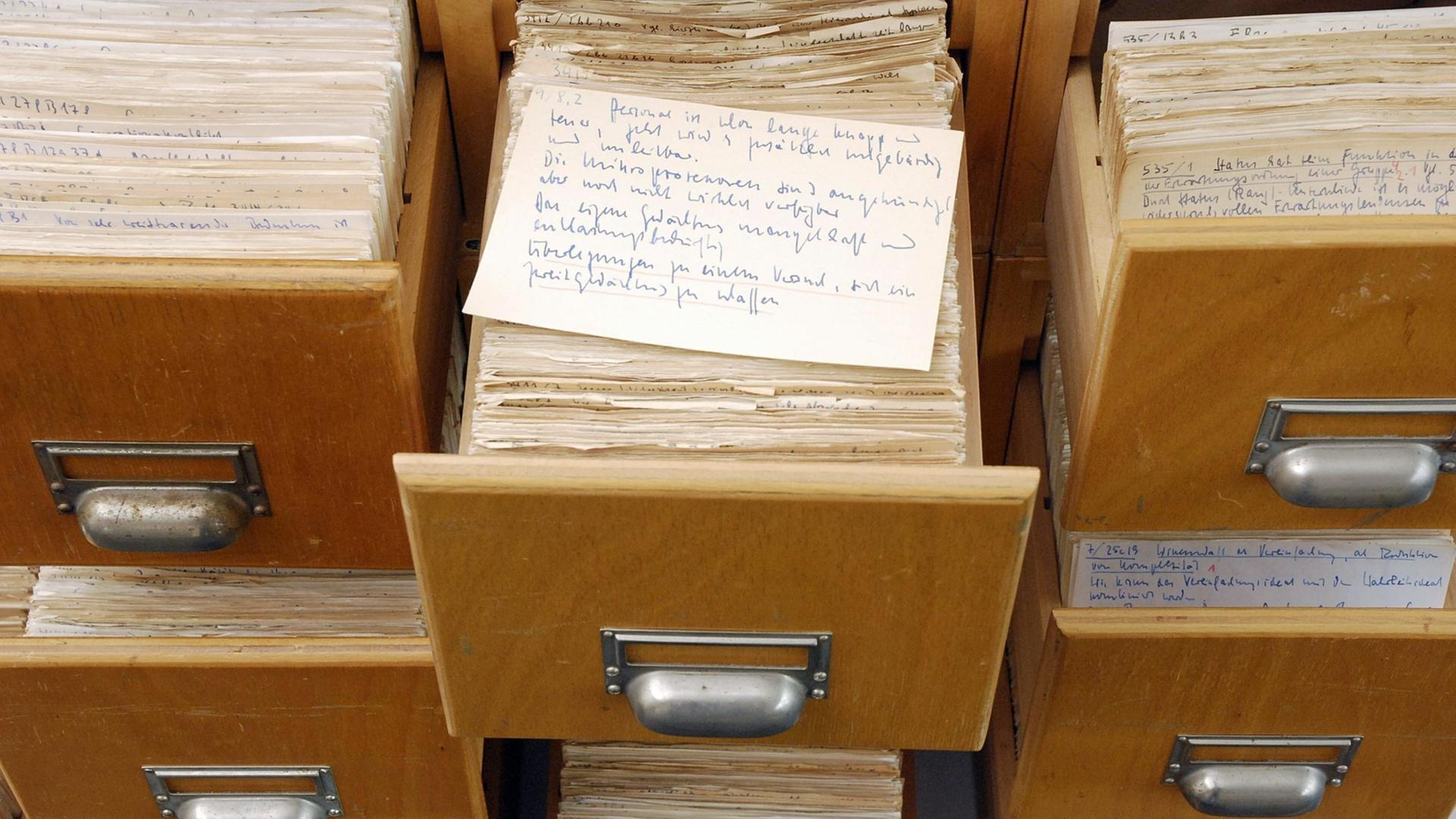 Eine handbeschriebne Karteikarte liegt auf einer von mehreren herausgezogenen Schubladen eines hölzernenen Karteikastenschrankes. Eine handbeschriebne Karteikarte liegt auf einer von mehreren herausgezogenen Schubladen eines hölzernenen Karteikastenschrankes.