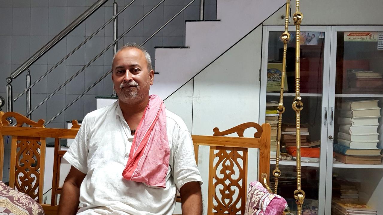 Porträt des indischen Gelehrten Parag Pathak in seiner Wohnung, im offenen weißen Hemd auf einer Bank mit geschnitzten Ornamenten sitzend.