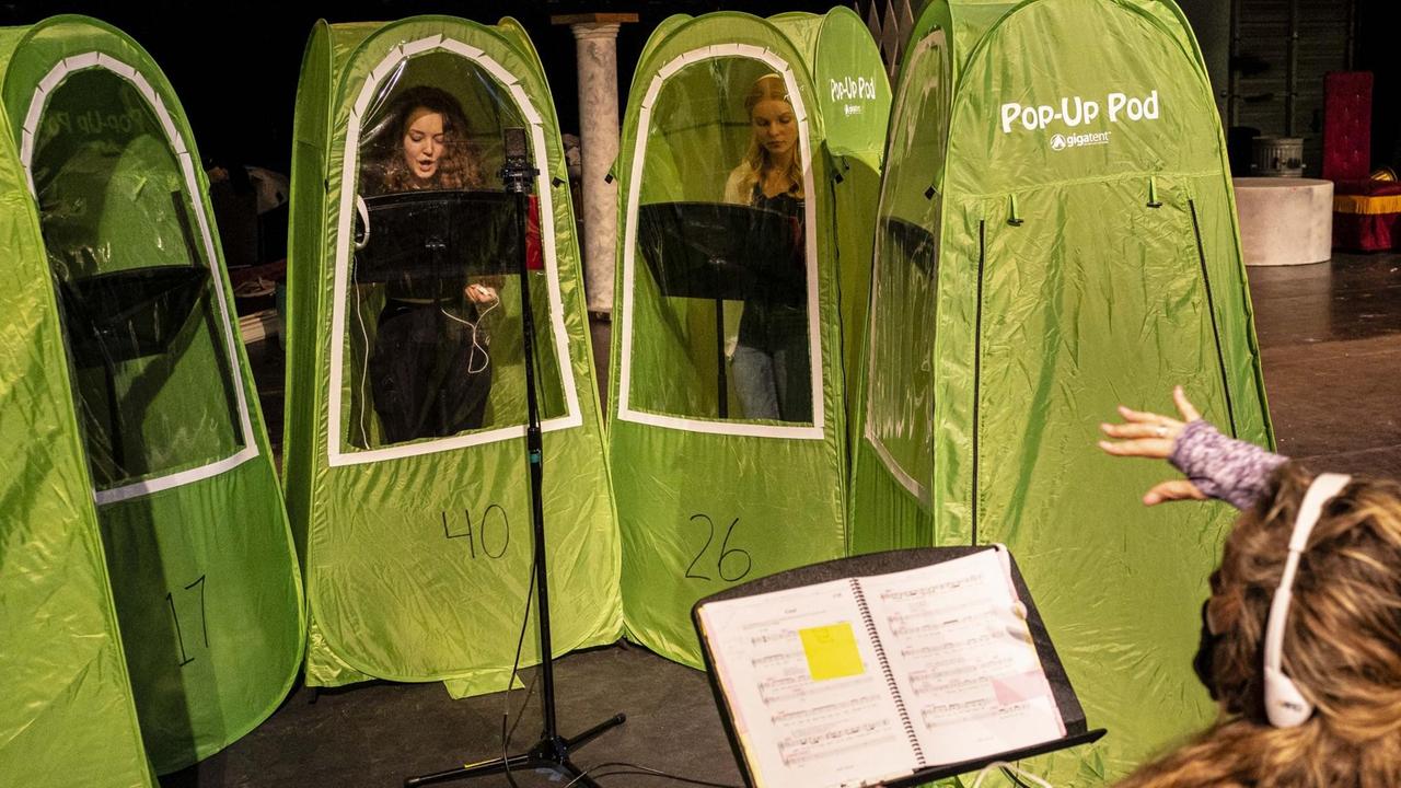 Junge Sängerinnen stehen in hellgrünen, hohen schmalen Zelten mit Sichtfenster und singen.