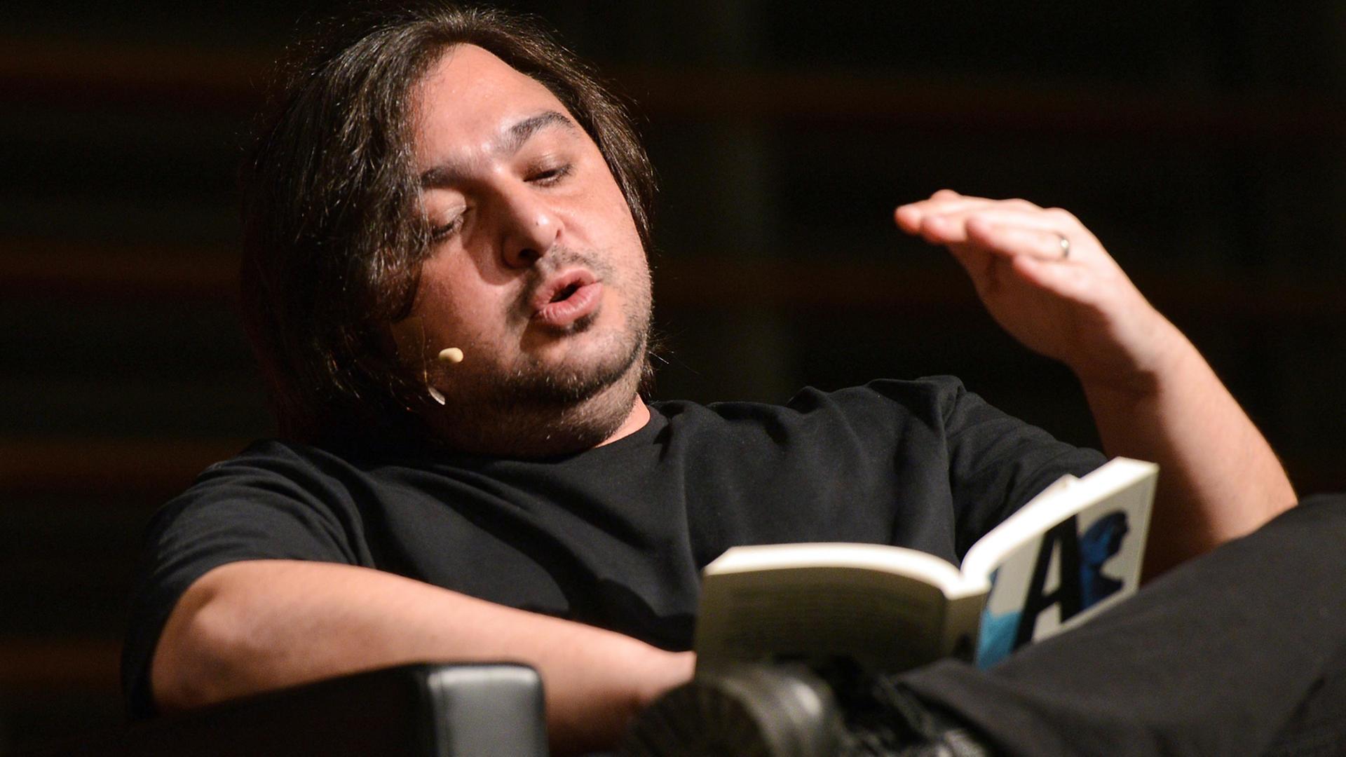 Der türkische Autor Hakan Günday sitzt in einem Sessel ud liest aus ein Buch vor Der türkische Autor Hakan Günday sitzt in einem Sessel ud liest aus ein Buch vor