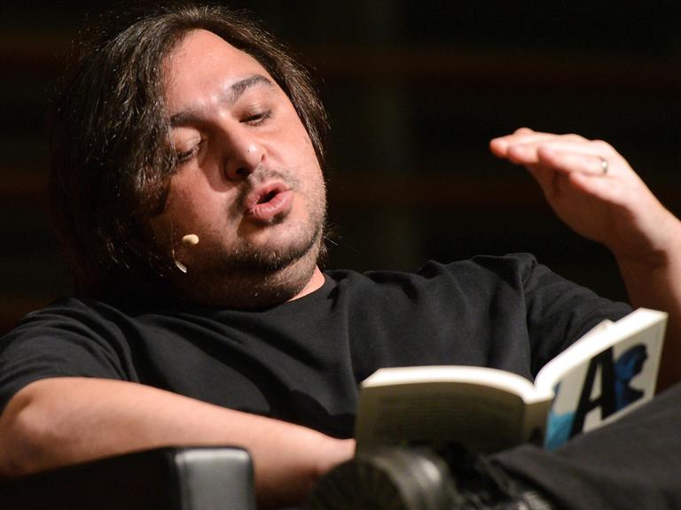 Der türkische Autor Hakan Günday sitzt in einem Sessel ud liest aus ein Buch vor