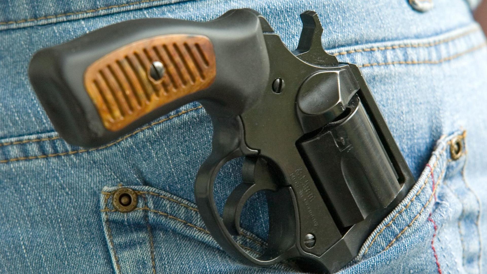 Ein Revolver Kaliber 9 mm ragt aus der Gesäßtasche einer Jeans-Hose Ein Revolver Kaliber 9 mm ragt aus der Gesäßtasche einer Jeans-Hose