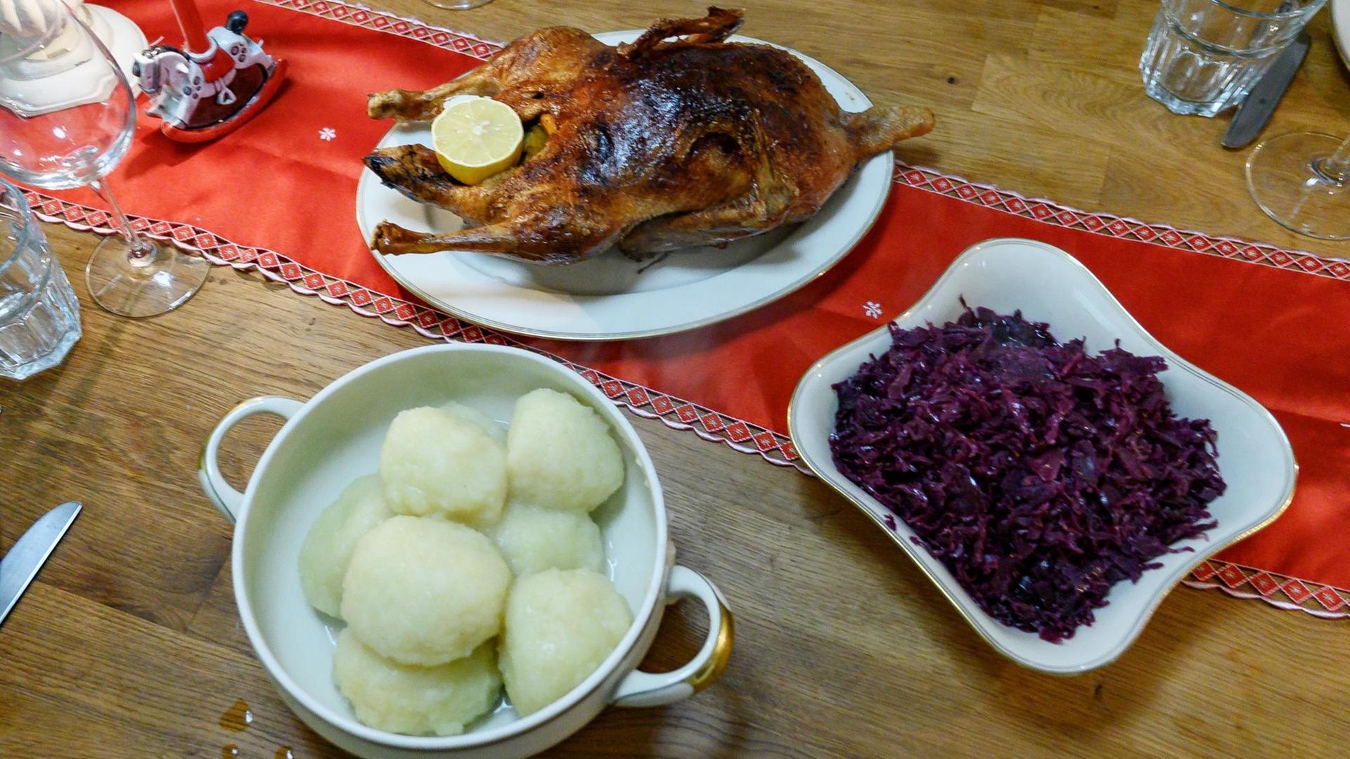 Eine gebratene Ente sowie Klöße und Rotkohl stehen auf einem gedeckten Tisch. Eine gebratene Ente sowie Klöße und Rotkohl stehen auf einem gedeckten Tisch.