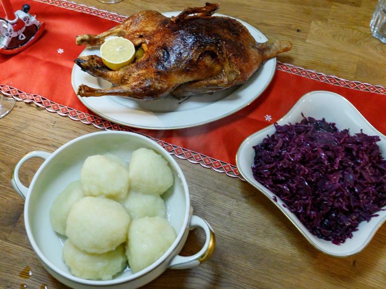 Eine gebratene Ente sowie Klöße und Rotkohl stehen auf einem gedeckten Tisch.