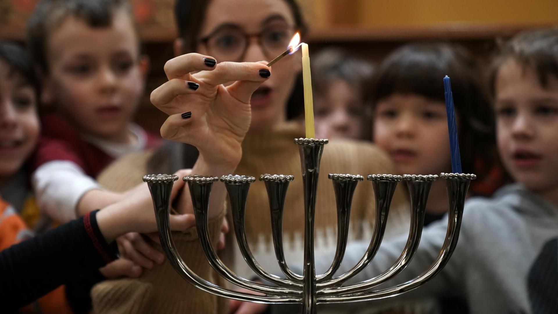 Eine Gruppe von Kindern und einer Frau zünden eine Chanukkah Kerze zum jüdischen Lichterfest am neunarmigen Leuchter an. Eine Gruppe von Kindern und einer Frau zünden eine Chanukkah Kerze zum jüdischen Lichterfest am neunarmigen Leuchter an.