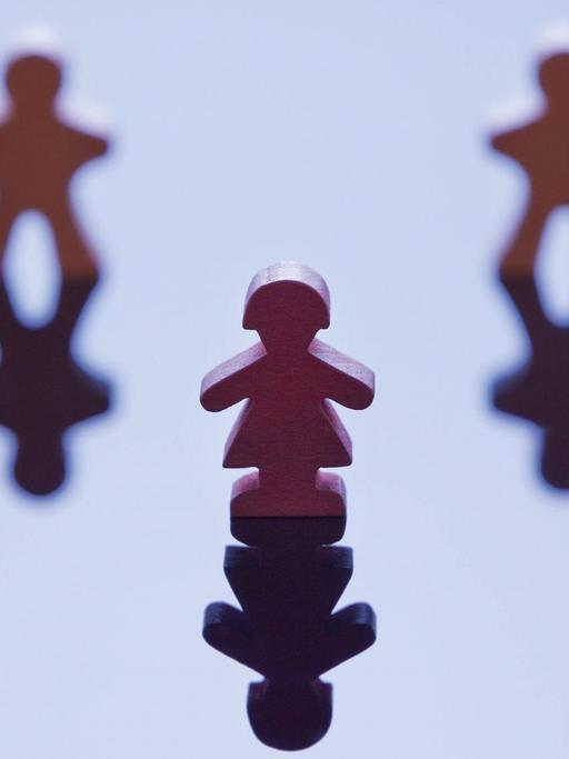 Vier männlich wirkende Spielfiguren stehen in einer Reihe mit einer Lücke in der Mitte, davor steht eine weiblich wirkende Figur.