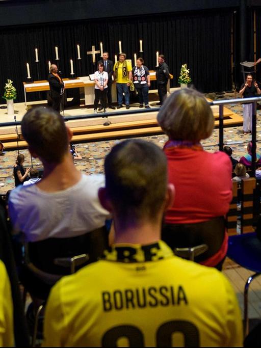 Fußballfans des Vereins Borussia Dortmund sitzen in der Kaiser-Wilhelm-Gedächtniskirche in Berlin während eines ökumenischen Gottesdienstes anlässlich des DFB-Pokalfinales der Männer im Rahmen des 36. Deutschen Evangelischen Kirchentages.