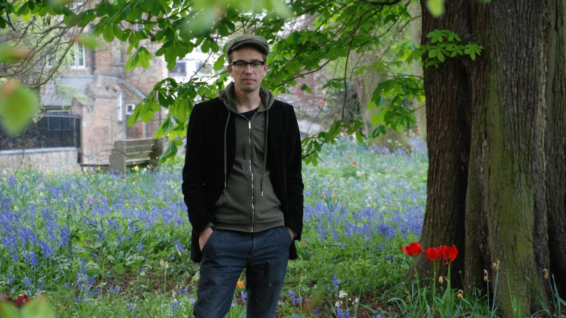 Der Historiker Sören Urbansky mit Schiebermütze und Brille steht auf einer Wiese unter einem Baum. Der Historiker Sören Urbansky mit Schiebermütze und Brille steht auf einer Wiese unter einem Baum.