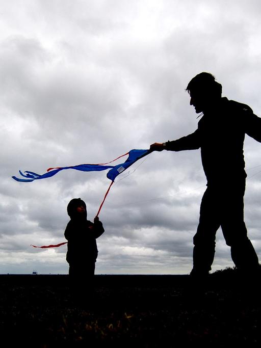 Ein Vater lässt am 16.03.2014 in Berlin auf dem Teufelsberg bei starkem Wind und dicht bewölktem Himmel mit seinem Sohn einen Drachen steigen.