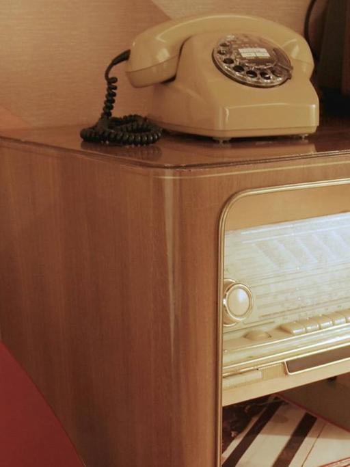 in Sessel neben einer Anrichte mit Fernsehgerät und Radio aus den 50er-Jahren
