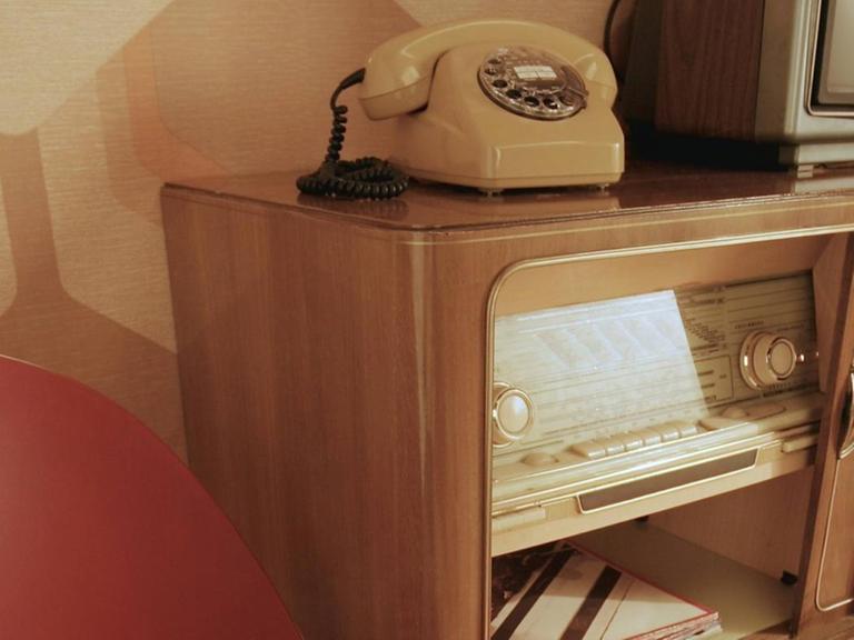 in Sessel neben einer Anrichte mit Fernsehgerät und Radio aus den 50er-Jahren