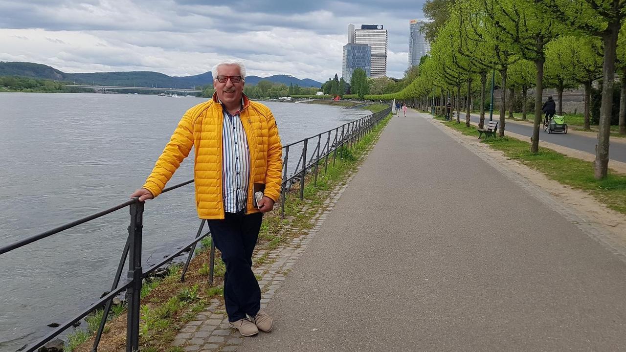 Heinz Hönig steht in gelber Jacke am Rheinufer. Im Hintergrund sind Hochhäuser des ehemaligen Regierungsviertels zu sehen. Heinz Hönig steht in gelber Jacke am Rheinufer. Im Hintergrund sind Hochhäuser des ehemaligen Regierungsviertels zu sehen.