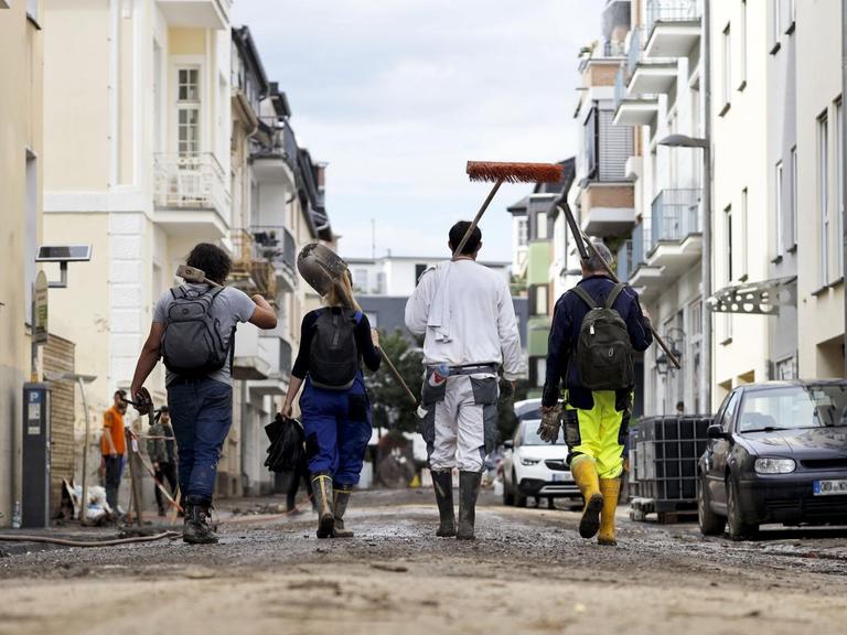 Im Bild gehen freiwillige Helfer in der Ortschaft Bad Neuenahr durch eine von dem Jahrhunderthochwasser zerstörte Straße.