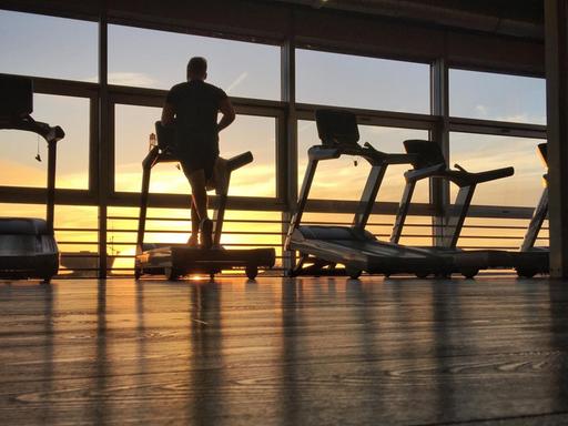 Sportler trainieren vor einer Fensterfront im Sonnenaufgang auf dem Laufband