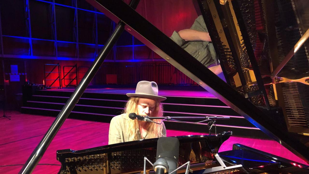 Ein Mann mit langen blonden Haaren und Hut sitzt an einem geöffneten Konzert-Flügel. Ein Mann mit langen blonden Haaren und Hut sitzt an einem geöffneten Konzert-Flügel.