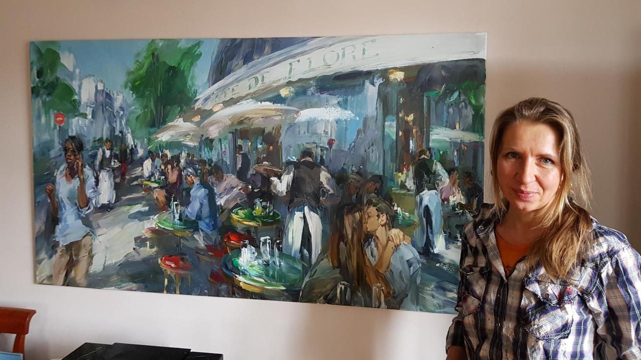 Malerin Ekaterina Zacharova steht vor ihrem Gemälde mit Landschaftsmotiv