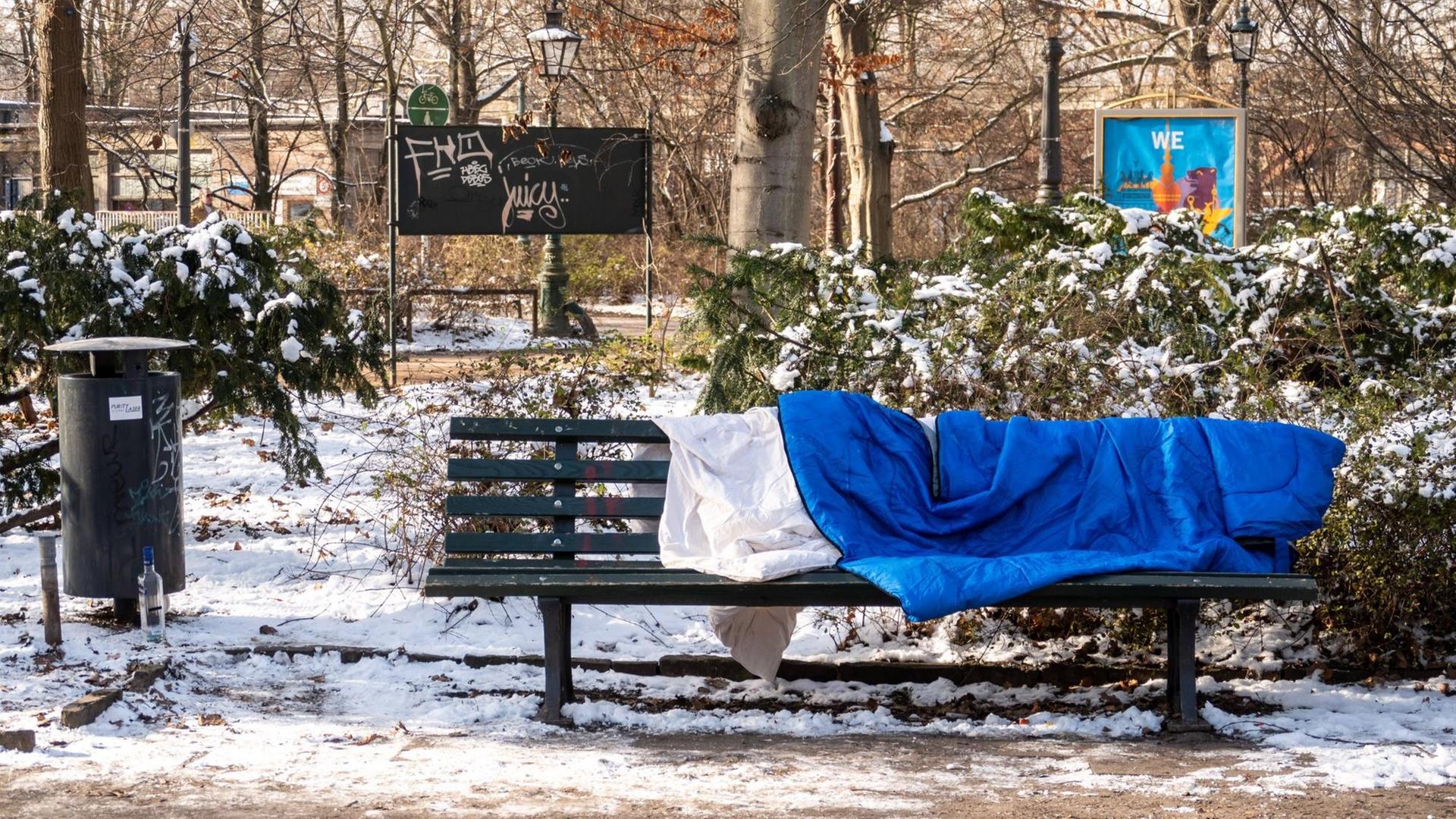 Ein Schlafsack liegt auf einer Bank im winterlichen Berlin. Im Großen Tiergarten liegt Schnee.