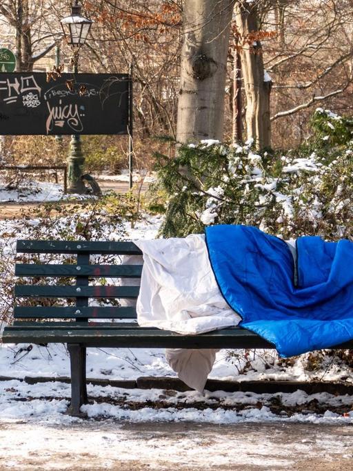 Ein Schlafsack liegt auf einer Bank im winterlichen Berlin. Im Großen Tiergarten liegt Schnee.