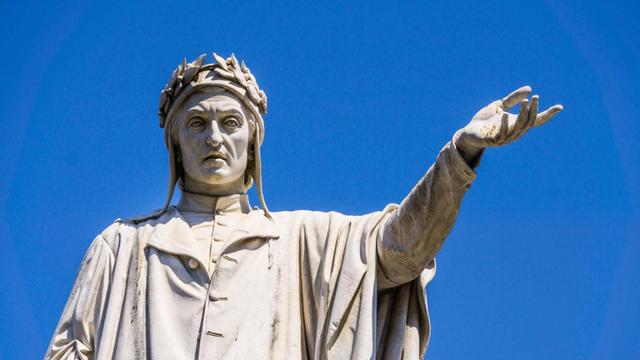 Die Dante-Alighieri-Skulptur in Neape vor blauem Himmel. Der Dichter streckt die linke Hand auf Schulterhöhe aus.