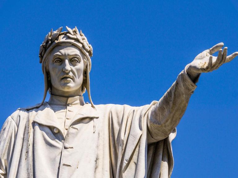 Die Dante-Alighieri-Skulptur in Neape vor blauem Himmel. Der Dichter streckt die linke Hand auf Schulterhöhe aus.