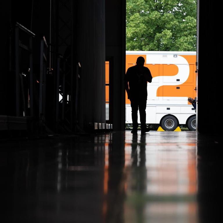 Ein Mann zeichnet sich auf dem Messegelände in einer Messehalle vor einem Übertragungswagen des ZDF als Silhouette ab