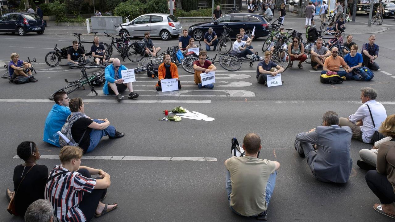 Mahnwache für eine getötete Fußgängerin in Berlin im Sommer 2018. Auf einer Kreuzung sitzen Menschen mit Blumen und Plakaten.