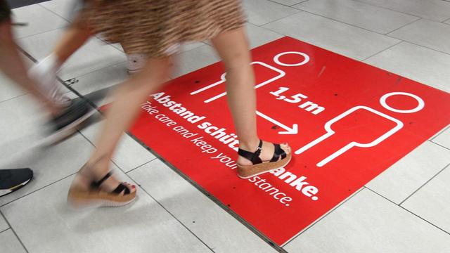 Großer Aufkleber mit Piktogramm und Aufschrift "Abstand von 1,50 Meter schützt" auf dem Boden im Hauptbahnhof Düsseldorf