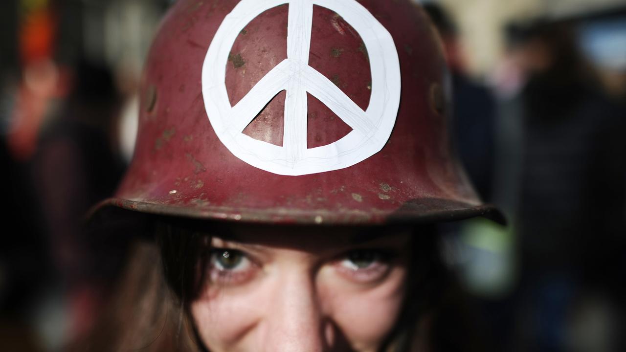 Eine junge Frau mit Peace-Zeichen auf einem Helm protestiert in München in der Innenstadt gegen die Sicherheitskonferenz.