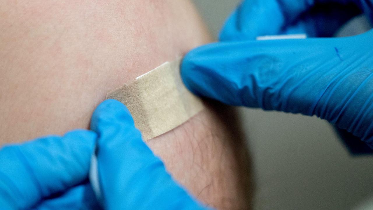 Ein Mitarbeiter des Impfzentrums des Klinikum Stuttgart klebt ein Pflaster auf den Oberarm eines Impflings. 