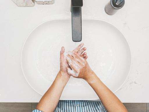 Blick von oben auf ein Waschbecken in dem sich eine Person die Hände wäscht.