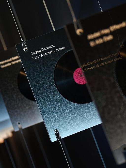 In einer Ausstellung sind mehrere Schellackplatten über Kopf aufgehängt. Ein Besucher betrachtet sie.