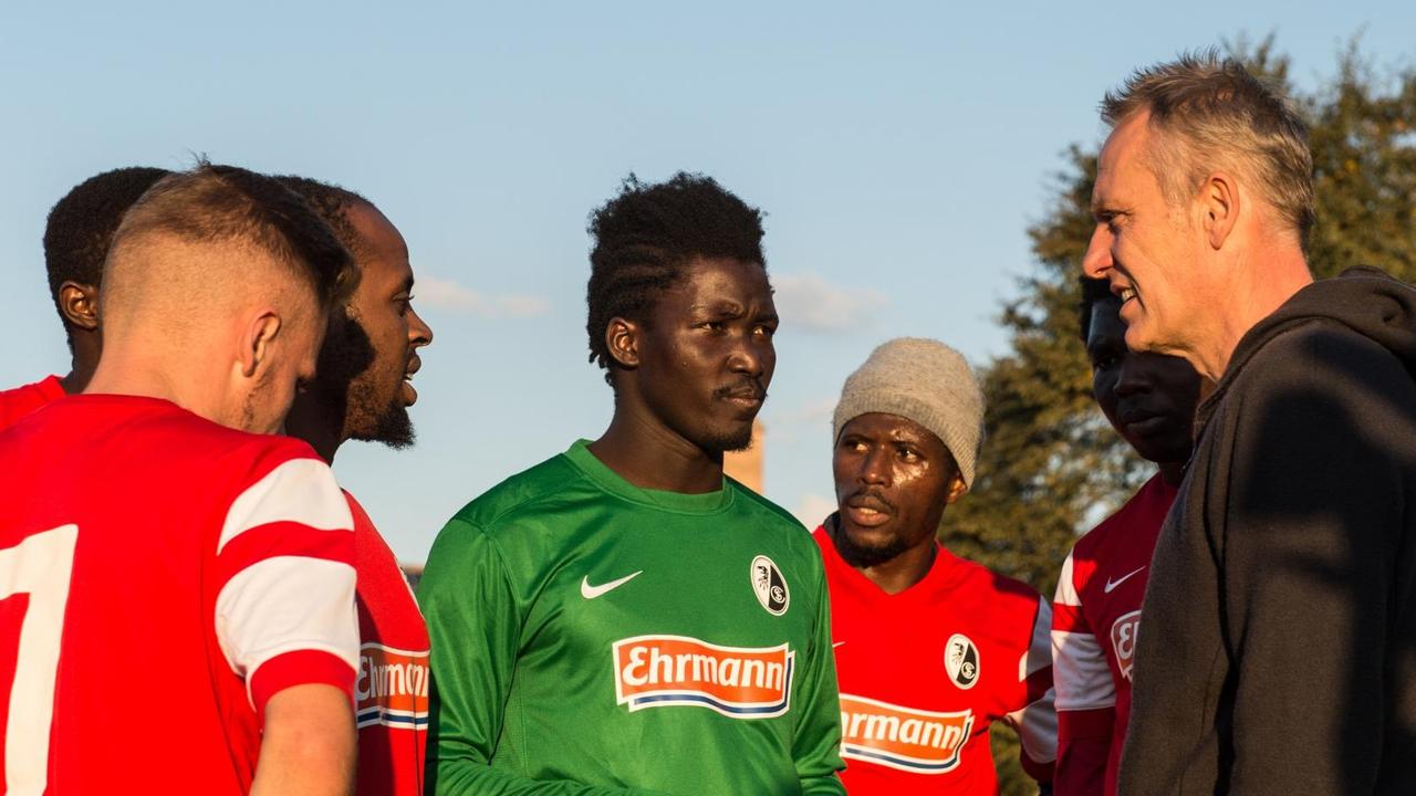 Flüchtlinge aus der Gemeinschaftsunterkunft Efringen-Kirchen sprechen am 29.09.2015 auf dem Sportplatz in Egringen (Baden-Württemberg) im Markgräflerland in Trikots des Bundesliga-Zweitligisten SC Freiburg mit Trainer Christian Streich (r). Flüchtlinge aus der Gemeinschaftsunterkunft Efringen-Kirchen sprechen am 29.09.2015 auf dem Sportplatz in Egringen (Baden-Württemberg) im Markgräflerland in Trikots des Bundesliga-Zweitligisten SC Freiburg mit Trainer Christian Streich (r).