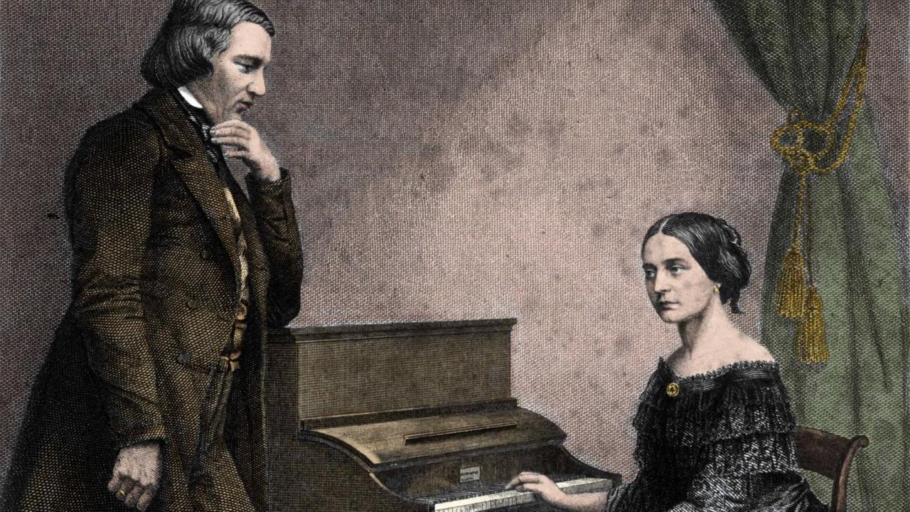 Der Komponist Robert Schumann steht neben seiner Ehefrau, der Pianistin und Komponistin Clara Schumann, sie sitzt am Klavier, er schaut sie an, sie schaut beiseite und scheint den Klängen nachzulauschen.