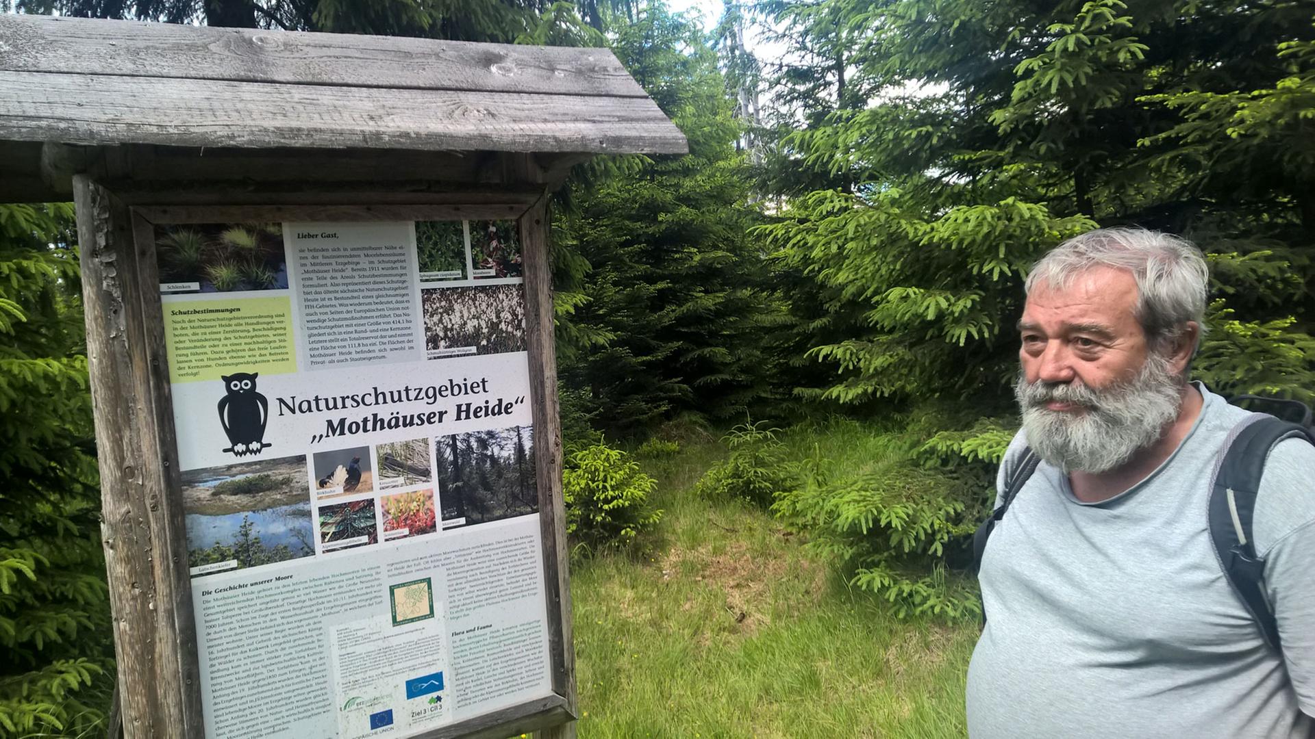 Ulrich Schuster, Mitbegründer des Naturschutzbundes im Erzgebirge, steht vor dem Schild, das auf die Kernzone des Naturschutzgebietes Mothäuser Heide in Sachsen hinweist.