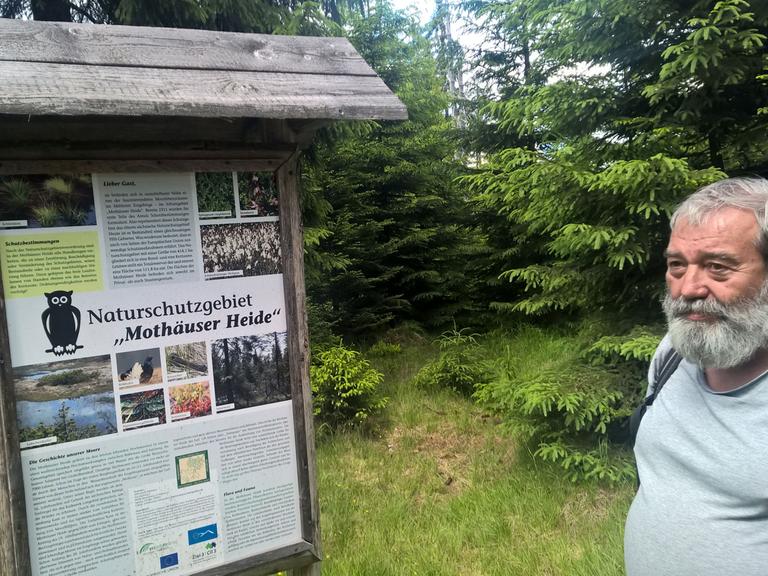 Ulrich Schuster, Mitbegründer des Naturschutzbundes im Erzgebirge, steht vor dem Schild, das auf die Kernzone des Naturschutzgebietes Mothäuser Heide in Sachsen hinweist.