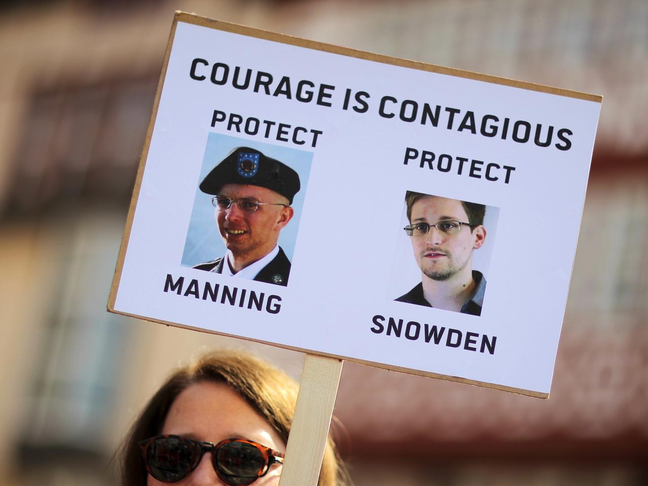 Eine Frau demonstriert in Frankfurt am Main und hält dabei ein Schild hoch, auf dem die Abbilder von Edward Snowden (r) und Bradley Manning zu sehen sind, da drüber die Aufschrift "courage ist contagious" (zu Deutsch: Courage ist ansteckend).