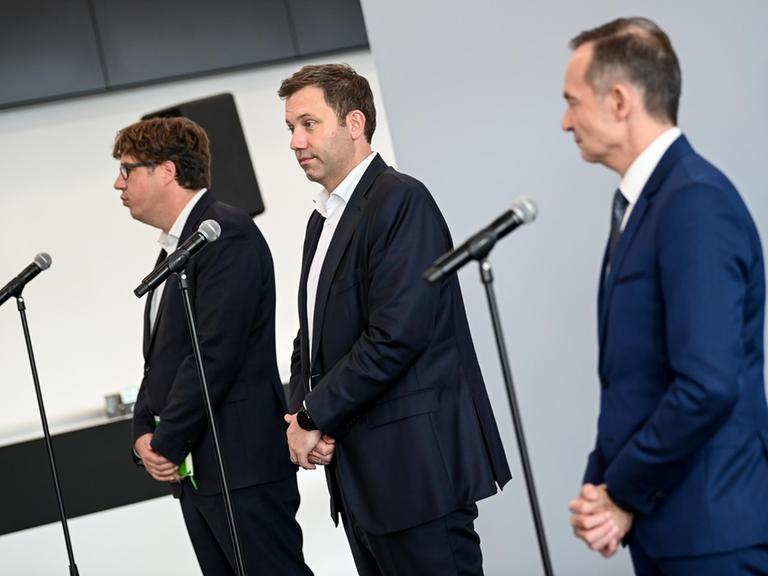 Michael Kellner, Lars Klingbeil und Volker Wissing stehen gemeinsam vor Mikrofonen . Vor der Seite fotografiert blicken sie in die Richtung der Pressevertreter.