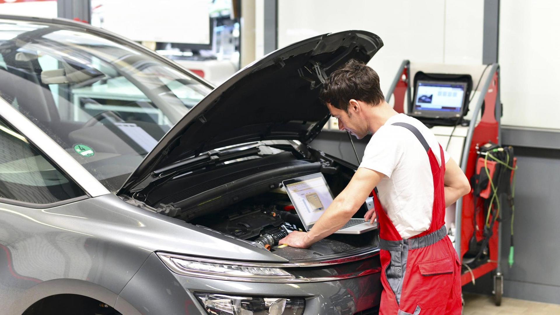 Ein Automechaniker mit einem Diagnosecomputer an einem Auto. Ein Automechaniker mit einem Diagnosecomputer an einem Auto.