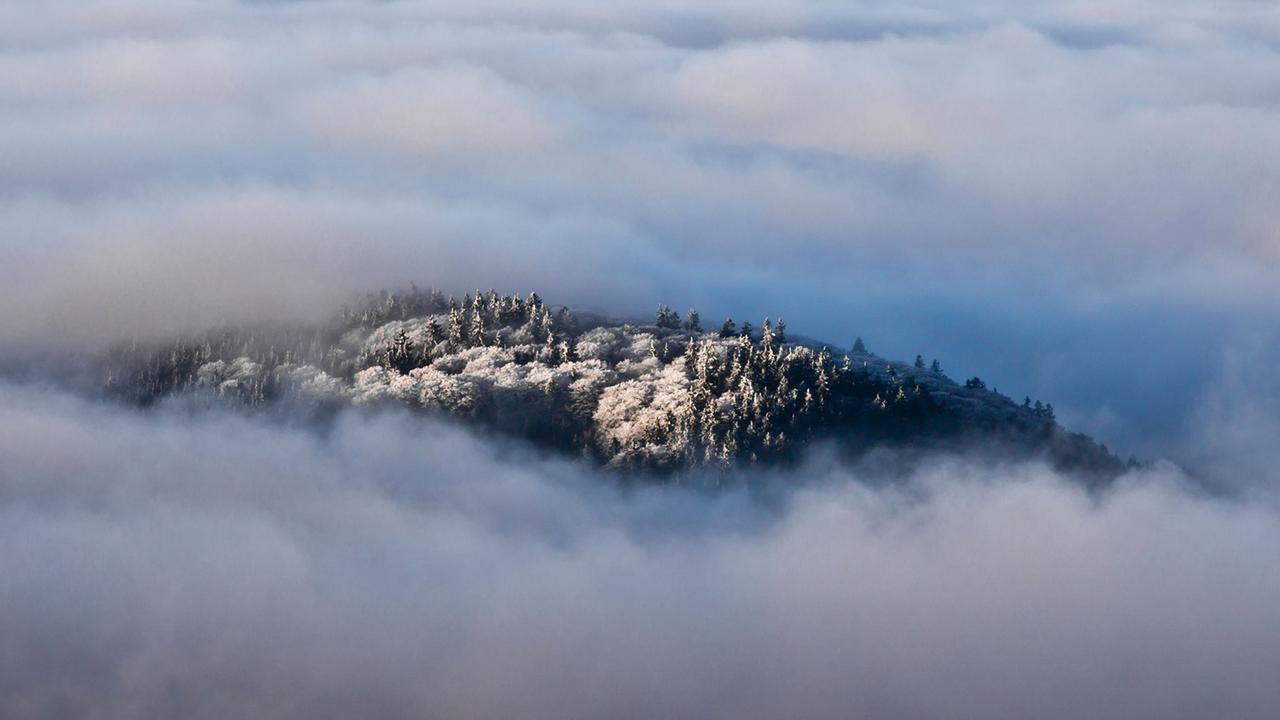 Ein einzelner Bergrücken schaut beim Blick vom Großen Feldberg im Taunus (Hessen) aus einem Wolkenmeer heraus, das die niedriger gelegene Landschaft bedeckt. Ein einzelner Bergrücken schaut beim Blick vom Großen Feldberg im Taunus (Hessen) aus einem Wolkenmeer heraus, das die niedriger gelegene Landschaft bedeckt.