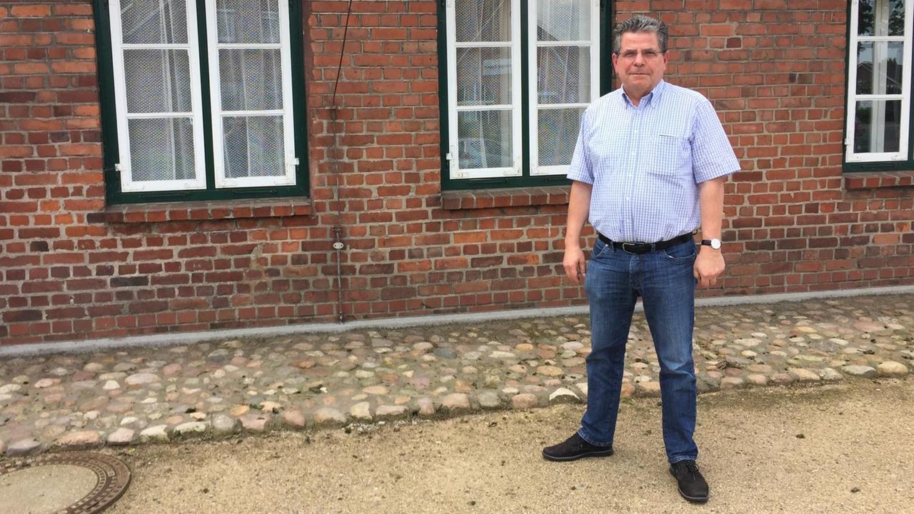 Ein Mann in einem hellen Hemd, dunklen Jeans und Brille steht vor einem Backsteinhaus. Der Mann heißt Walter Lorenzen, er ist stellvertretender Bürgermeister des Ortes Appen bei Hamburg. Ein Mann in einem hellen Hemd, dunklen Jeans und Brille steht vor einem Backsteinhaus. Der Mann heißt Walter Lorenzen, er ist stellvertretender Bürgermeister des Ortes Appen bei Hamburg.