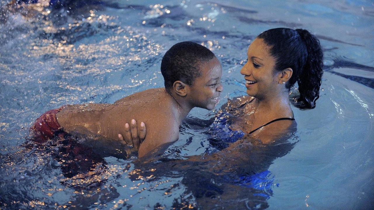 Maritza Correia hält einen neun Jahre alten, Schwarzen Jungen im Wasser fest, beide lächeln