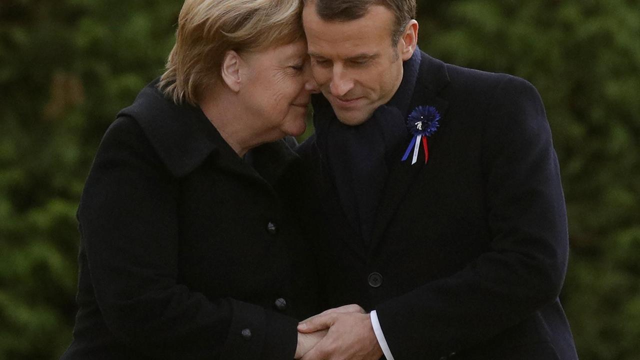 Merkel legt ihren Kopf mit geschlossenen Augen an den Kopf Macrons. Merkel legt ihren Kopf mit geschlossenen Augen an den Kopf Macrons.