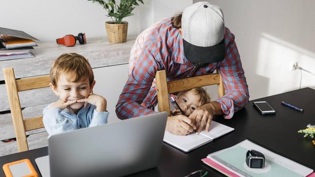 Klassenzimmer und Arbeitsplatz vereint in der Küche – ein Mann mit zwei Kindern mit Unterlagen und Laptop
