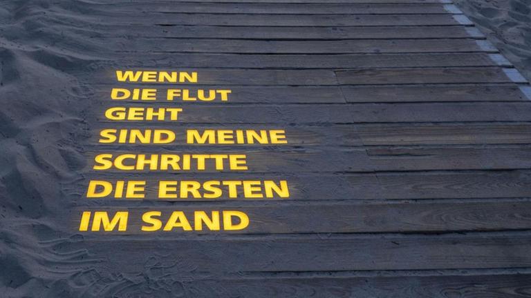 Eine Lichtinstallation von Jan Philip Scheibe mit einem Gedicht auf der Insel Langeoog: "Wenn die Flut geht, sind meine Schritte die ersten im Sand".