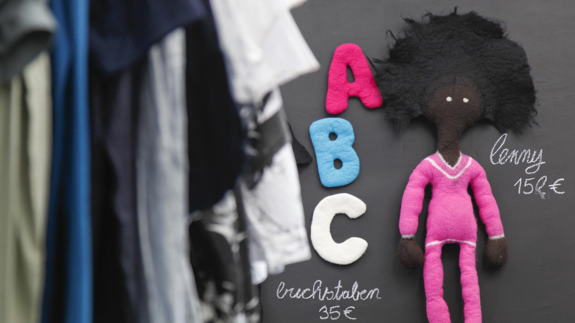 Neben einem Ständer mit Kleidung hängt in einer Boutique in München eine Spielzeugpuppe aus Öko-Wolle. Neben einem Ständer mit Kleidung hängt in einer Boutique in München eine Spielzeugpuppe aus Öko-Wolle.