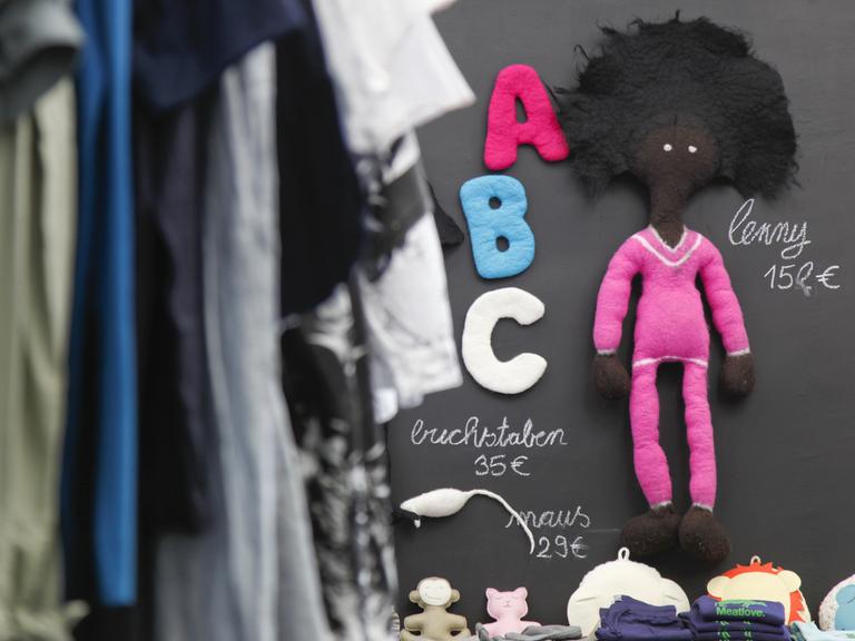 Neben einem Ständer mit Kleidung hängt in einer Boutique in München eine Spielzeugpuppe aus Öko-Wolle.