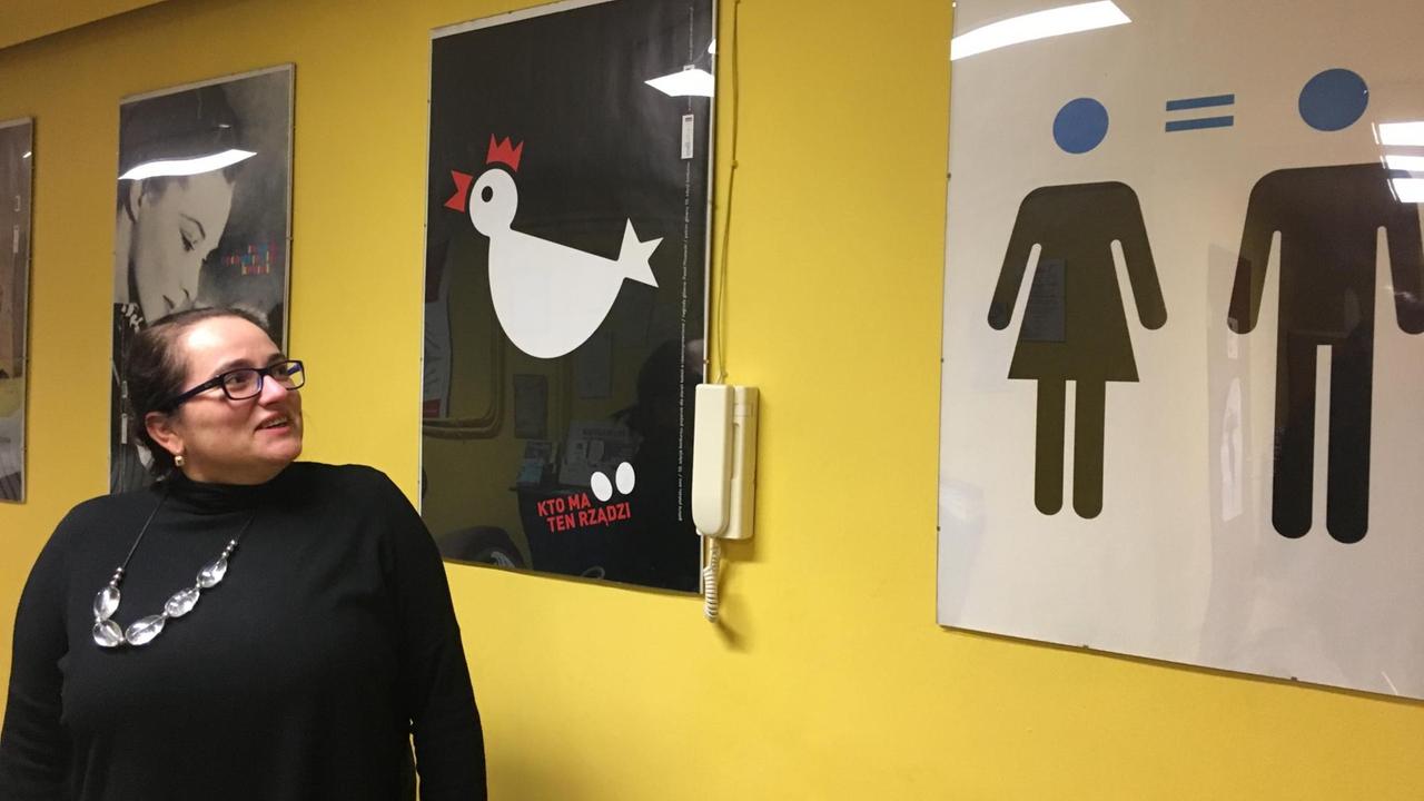 Gelbe Wand, Poster mit Frauenthemen, davor eine Frau, die di ePoster anlacht Gelbe Wand, Poster mit Frauenthemen, davor eine Frau, die di ePoster anlacht