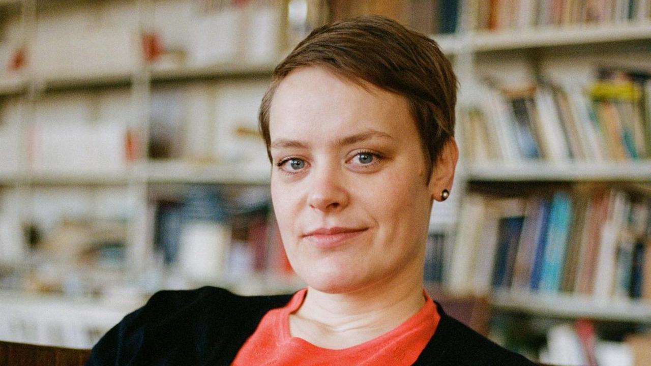 Hanna Engelmeier sitzt vor einer Bücherwand. Sie trägt ein hellrotes Oberteil und eine schwarze Jacke und schaut in die Kamera. Das Haar trägt sie kurz mit Seitenscheitel. Hanna Engelmeier sitzt vor einer Bücherwand. Sie trägt ein hellrotes Oberteil und eine schwarze Jacke und schaut in die Kamera. Das Haar trägt sie kurz mit Seitenscheitel.