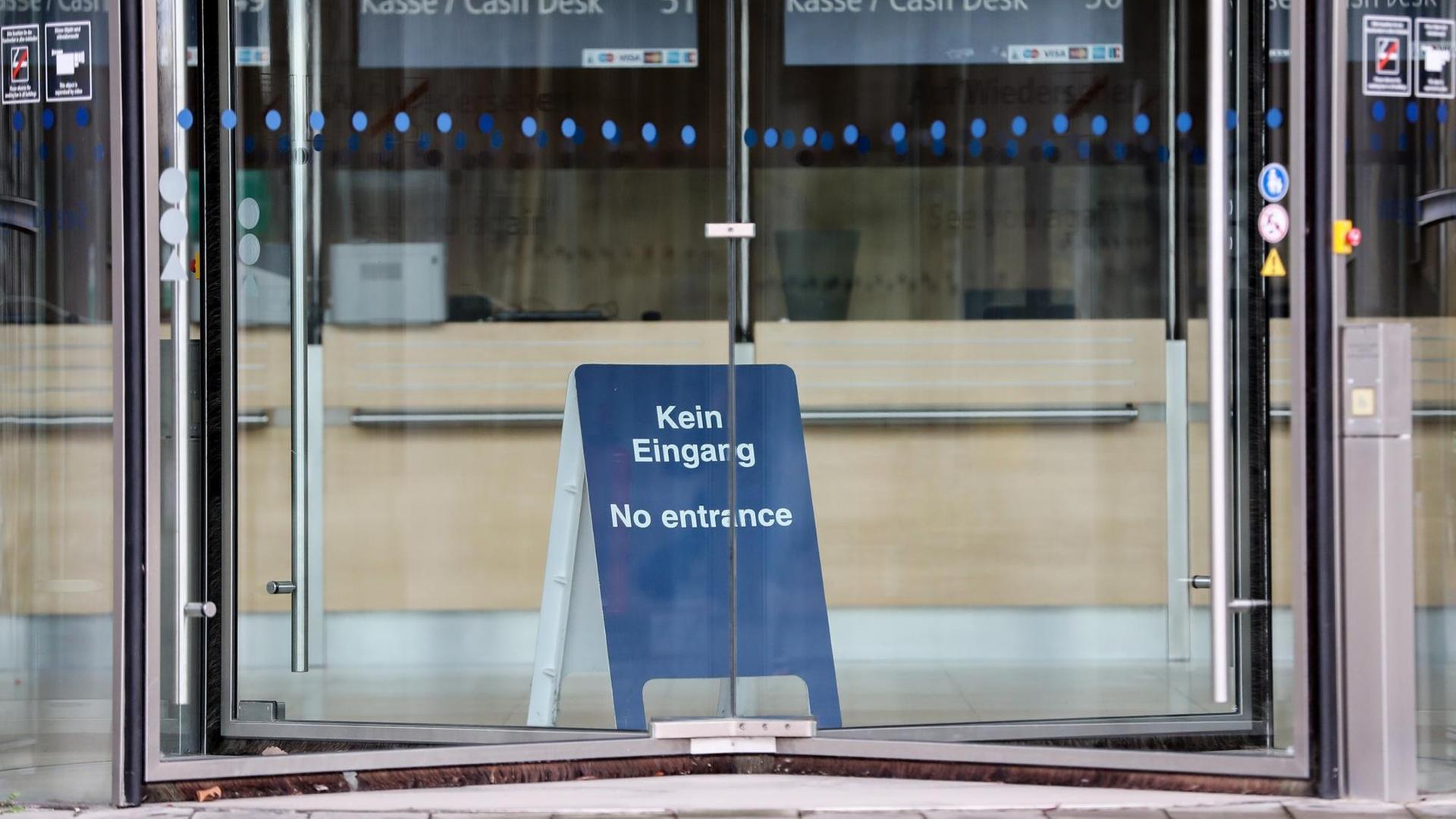 Durch eine Drehtür ist ein blaues Aufstellschild mit der Aufschrift 'Kein Eingang, No entrance' zu sehen. Im Hintergrund sind die leeren Kassenplätze. Durch eine Drehtür ist ein blaues Aufstellschild mit der Aufschrift 'Kein Eingang, No entrance' zu sehen. Im Hintergrund sind die leeren Kassenplätze.