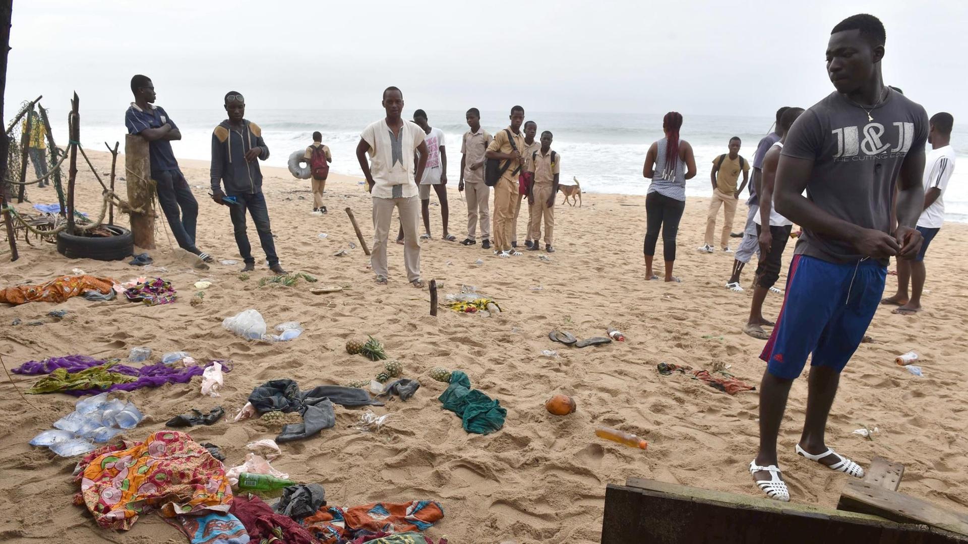 Man sieht Menschen an einem Strand, es liegen Kleidungsstücke im Sand. Man sieht Menschen an einem Strand, es liegen Kleidungsstücke im Sand.